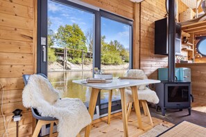 Een chalet met houten inrichting, een eettafel met stoelen, een open haard en een groot raam met uitzicht op een waterpartij.