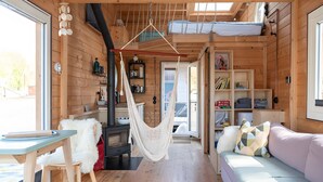 A cozy cabin interior with a hammock, a sofa, a dining table, and a kitchen area. - Holiday Home 'Besonderes Tiny Hausboot Marianne' with Private Terrace and Wi-Fi (Hamburg)