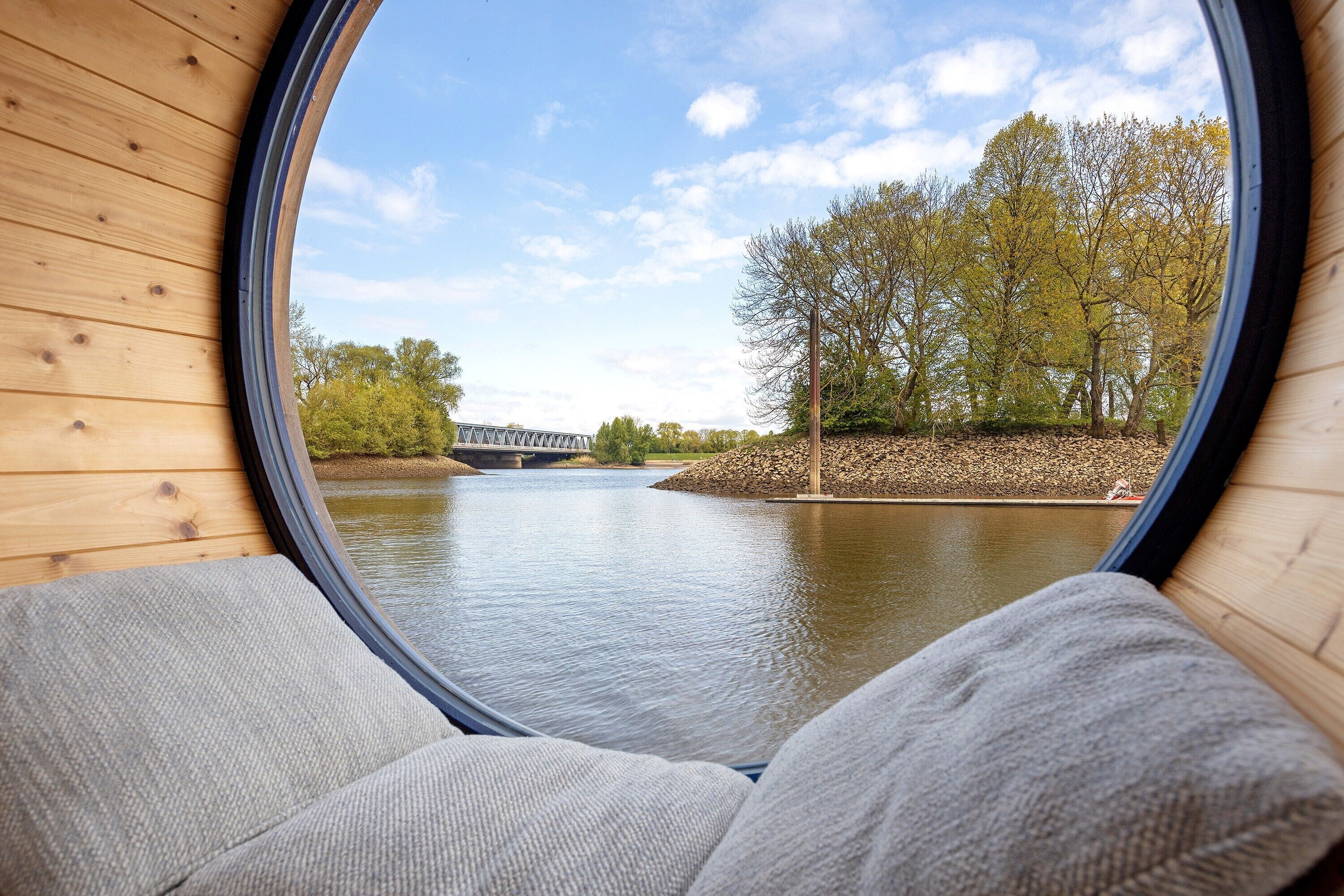 A view through a window of a wooden cabin with a river and bridge in the background.