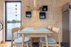 A wooden interior with a table and chairs, a view of a bridge, and shelves with items.