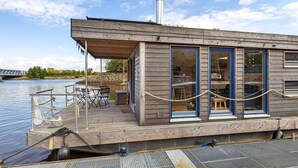 Una casa flotante de madera con cubierta techada, una chimenea y un muelle.