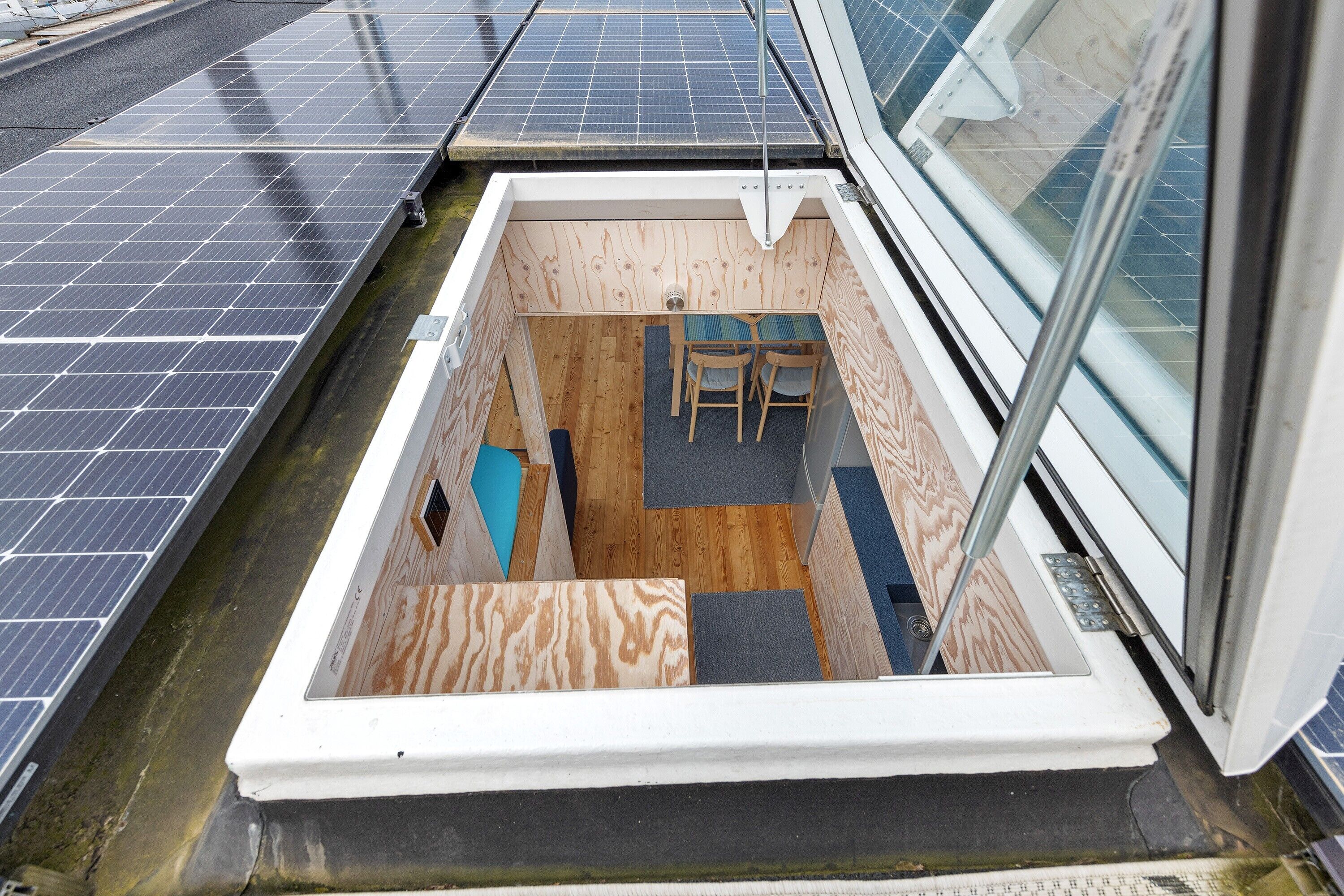 Ein schmaler Raum mit einem kleinen Tisch und zwei Stühlen, einem Fenster und Solaranlagen außen.