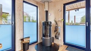 Un interior moderno con estufa de leña, ventanas amplias y vistas al exterior.