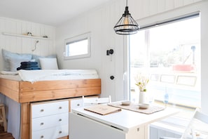 Une pièce comprenant un lit, un bureau, une chaise, une fenêtre et un luminaire suspendu.