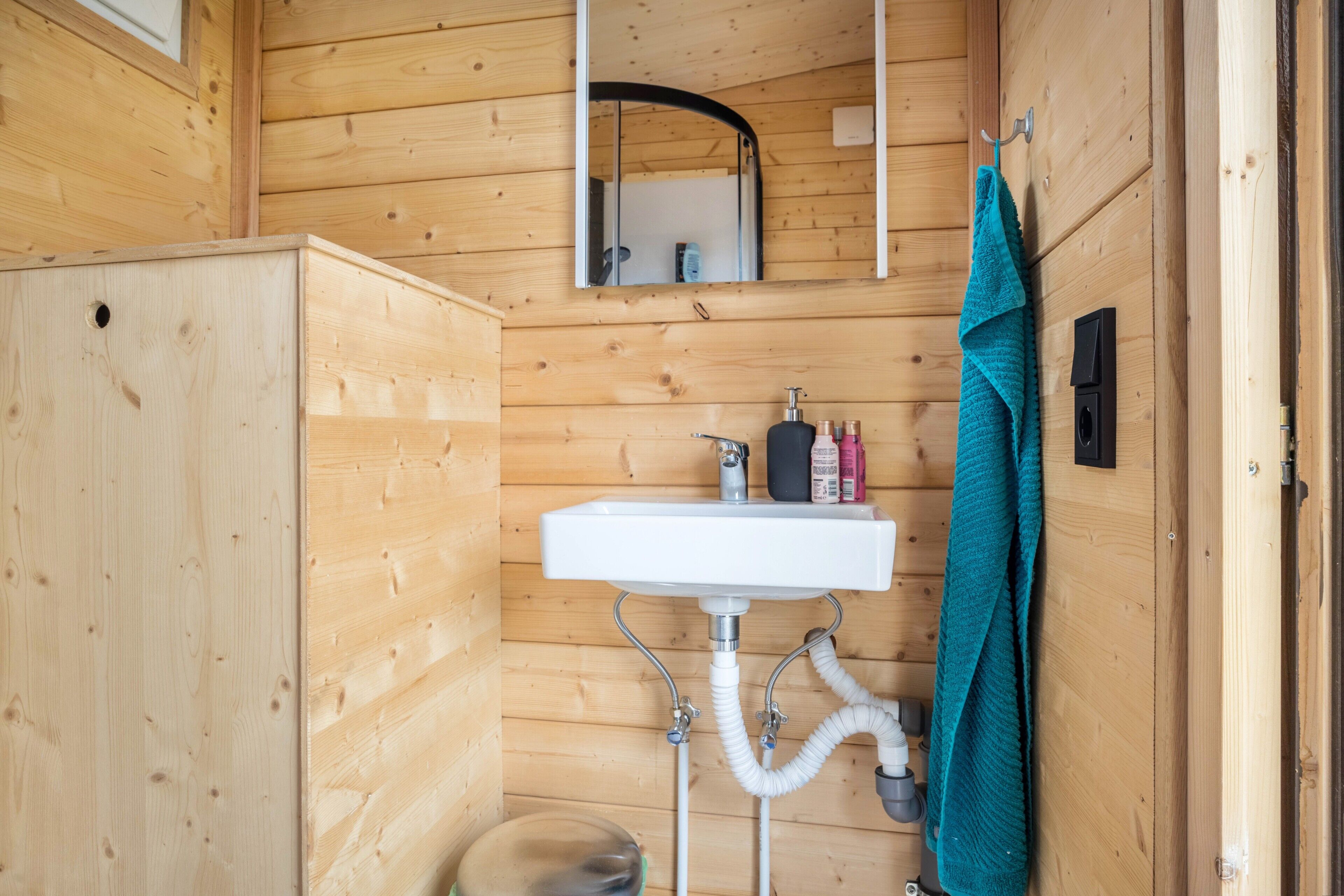 Een houten badkamer in een vakantiehuisje, met een wastafel, spiegel en handdoekhouder.