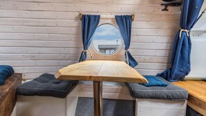 A compact room with a wooden table, two cushioned seating areas, a mirror, and curtains.