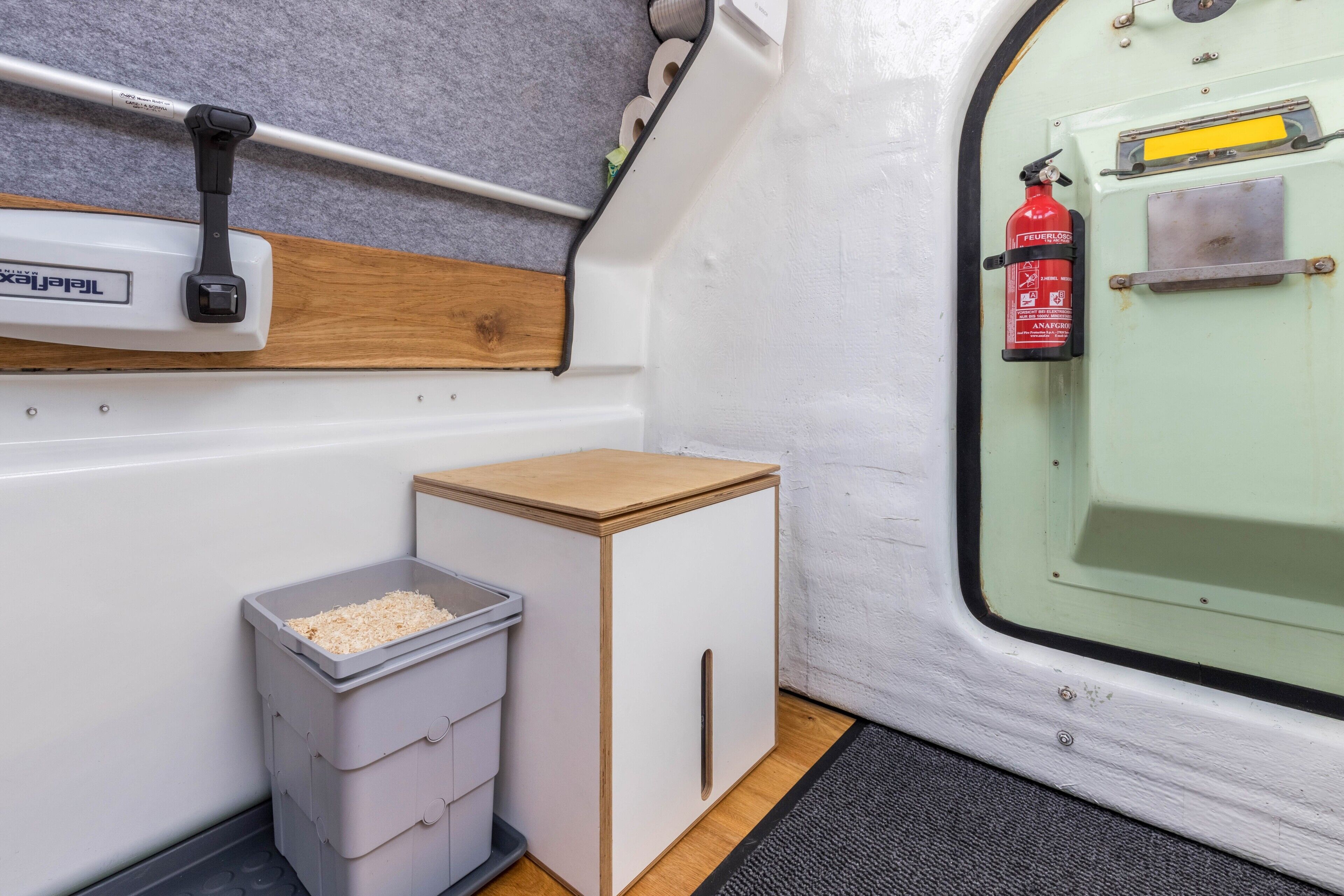 Een compacte kitchenette met een prullenbak, een klein kastje en een brandblusser aan de muur.
