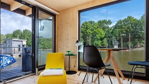 Una habitación moderna con un ventanal grande, una silla amarilla, una silla negra y una mesita.