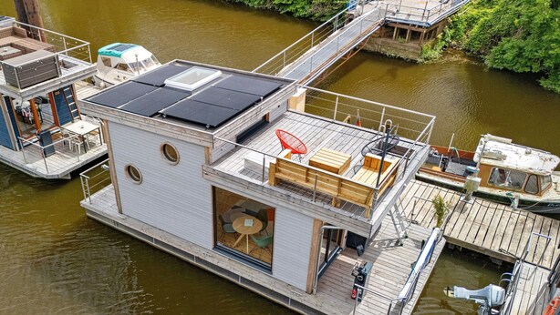Una casa flotante con terraza, zona de estar al aire libre cubierta y panel solar.