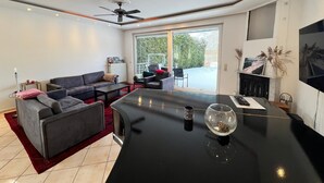 Un moderno salón con una mesa de comedor negra, sofás grises y un ventilador de techo.