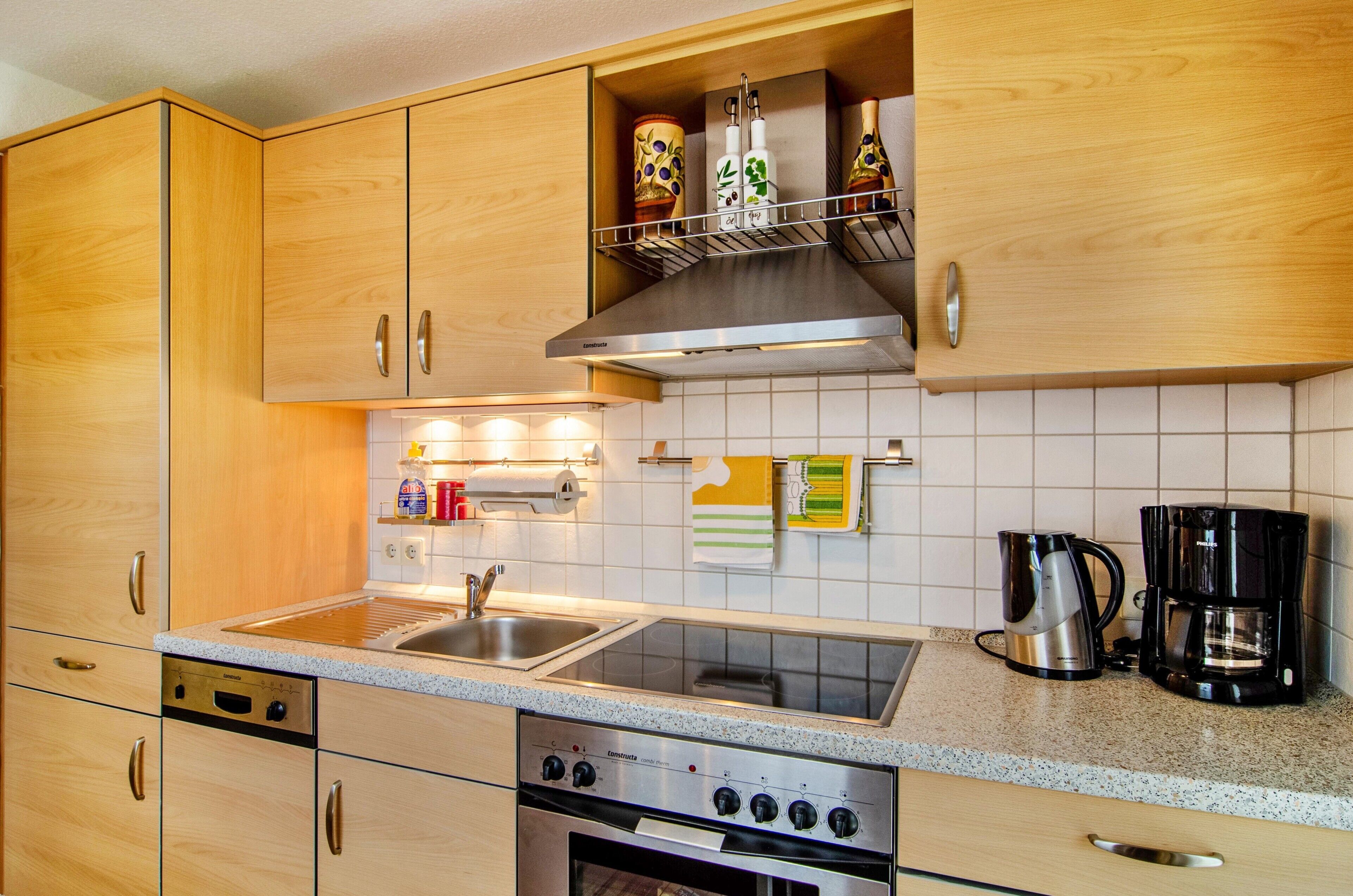 A kitchen with wooden cabinets, a stainless steel sink, a stove, and a coffee maker.
