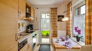 Eine Küche mit Holzausstattung, einem Esstisch mit Tee-Service und einem Fenster mit Vorhängen.