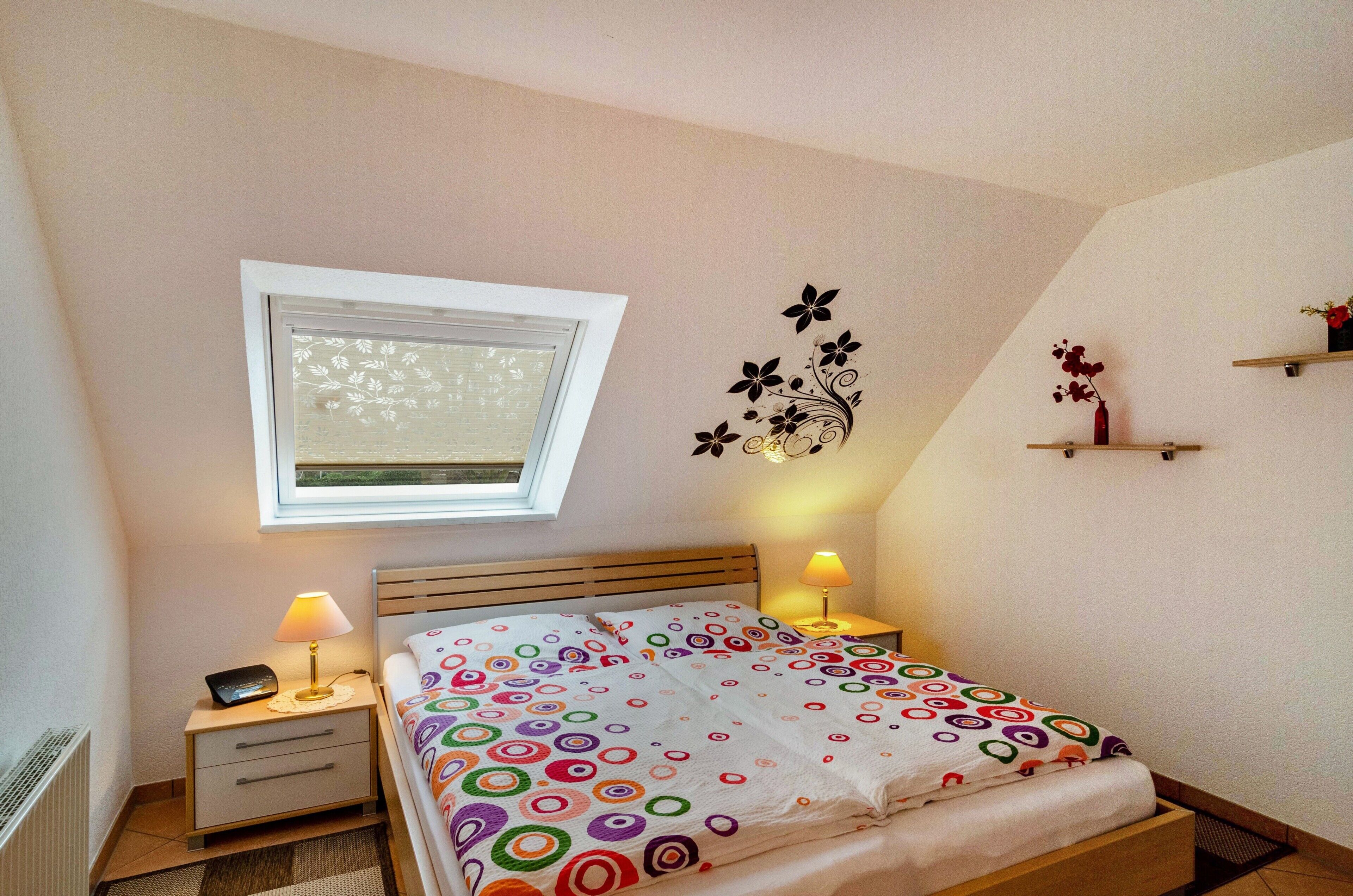 Una camera da letto con un letto, due comodini con lampade, una finestra e decorazioni alle pareti.