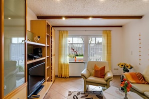 Una sala de estar con sofá, sillón, televisor y estantería.