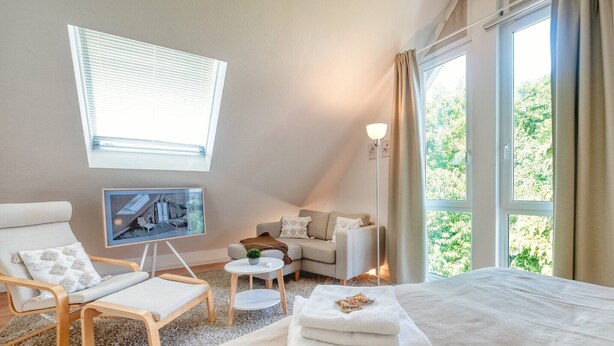 A hotel room with a bed, a chair, a small table, a TV, and large windows. - Holiday Apartment 'Iris und Uwe' with Mountain View, Private Terrace and Wi-Fi (Markdorf)
