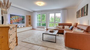 A spacious living room with a large TV, a sofa, a coffee table, and a view of greenery outside. - Holiday Apartment 'Iris und Uwe' with Mountain View, Private Terrace and Wi-Fi (Markdorf)