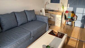 Una sala de estar moderna con un sofá gris, una mesa de centro de madera, un sillón colorido y un escritorio con una computadora.