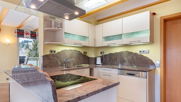 Una cocina moderna con encimeras de granito, estufa empotrada, armarios blancos y salpicadero de piedra.