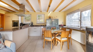 Una cocina moderna con una isla central, vigas de madera en el techo y un comedor con sillas y una mesa.