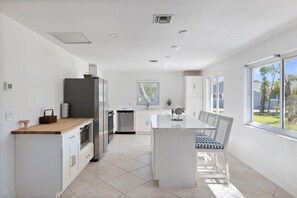 A modern kitchen with white cabinetry, a wooden countertop, and a dining area with a table and chairs.