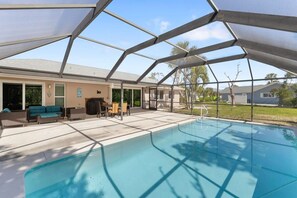 Una piscina al aire libre techada con zona de patio, que incluye asientos y una mesa.