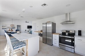 A modern kitchen with a central island, stainless steel appliances, and a dining area with a blue and white patterned bench.