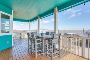Uma área externa coberta com deck de madeira, uma mesa com cadeiras e vista para a praia.