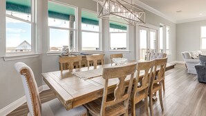 Uma sala de jantar com mesa e cadeiras de madeira, um lustre e janelas amplas com vista.