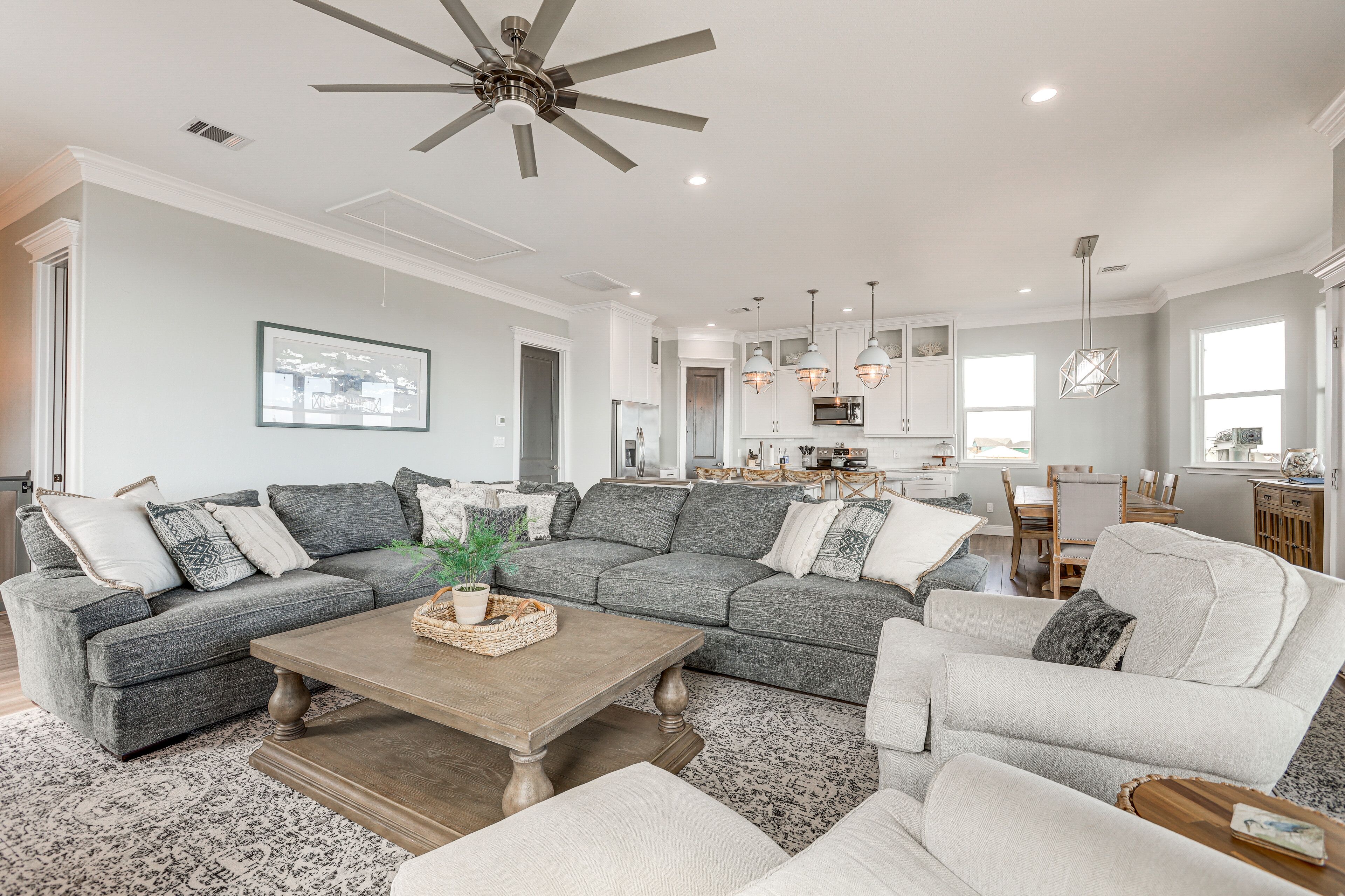 A spacious living room with a gray sectional sofa, a wooden coffee table, and a ceiling fan.