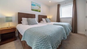Une chambre d’hôtel avec deux lits, une table de chevet, une lampe, un tableau et une fenêtre avec des rideaux.