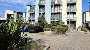 Un immeuble résidentiel à plusieurs étages, doté de balcons, d’une cour pavée et de quelques espaces verts.