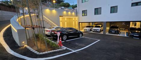 Un aparcamiento con coches, un edificio de varios pisos y una escalera que sube a un nivel superior.