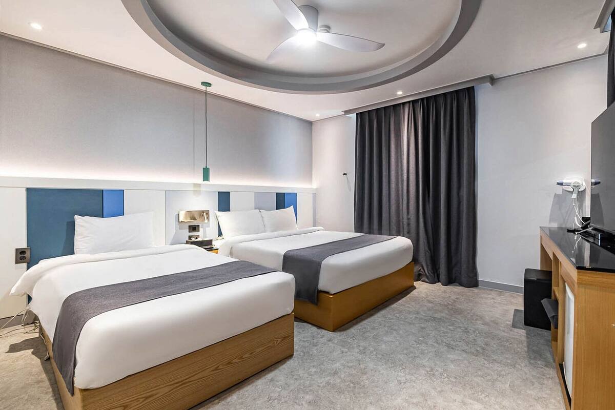 A hotel room with two beds, a TV, a desk, and a ceiling fan.