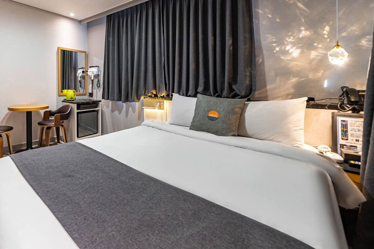 A hotel room with a large bed, a desk with chairs, a mirror, and a wardrobe with clothes hanging.