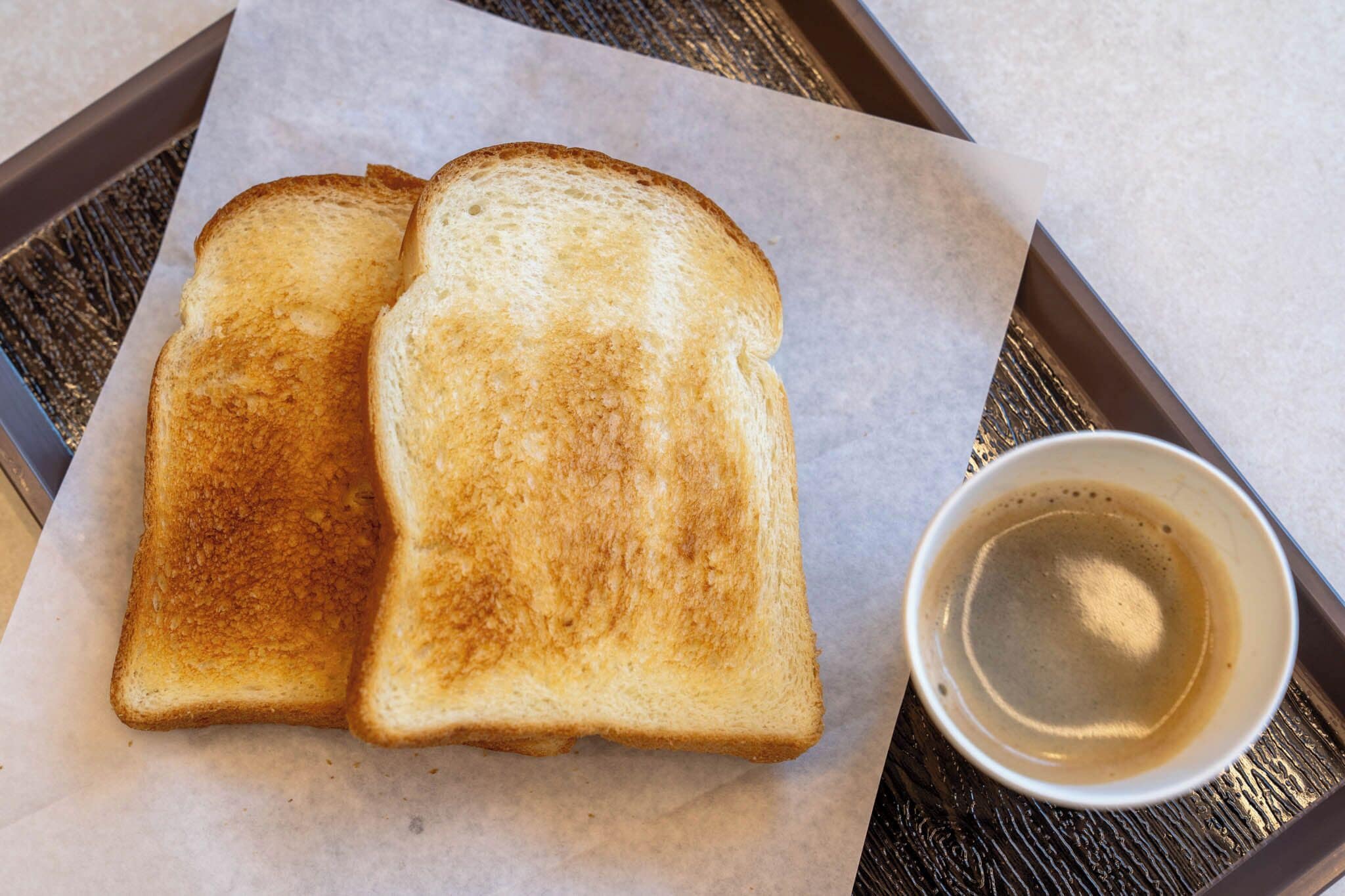 Duas fatias de pão tostado numa bandeja com uma xícara de café.