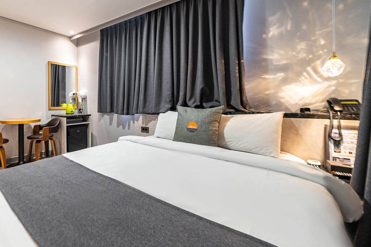 A modern hotel room with a large bed, a desk with chairs, a mirror, and a telephone.