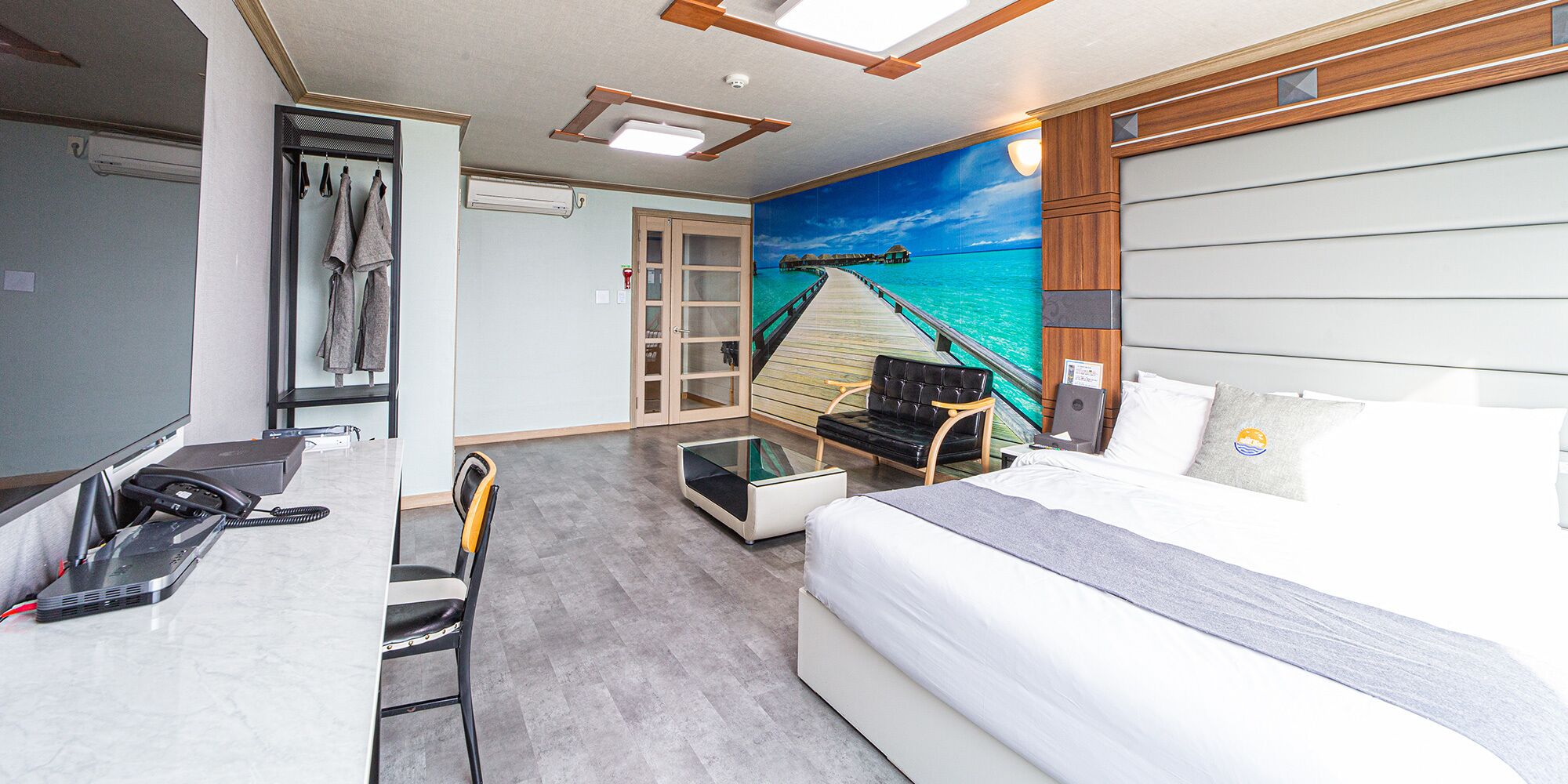 Habitación de hotel con cama, escritorio con computadora, silla, una mesita y un cuadro con una playa.
