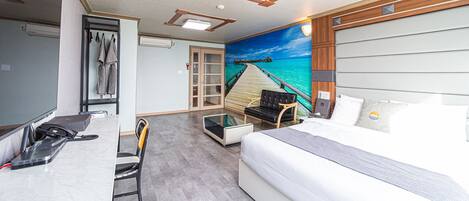 Habitación de hotel con cama, escritorio con computadora, silla, una mesita y un cuadro con una playa.