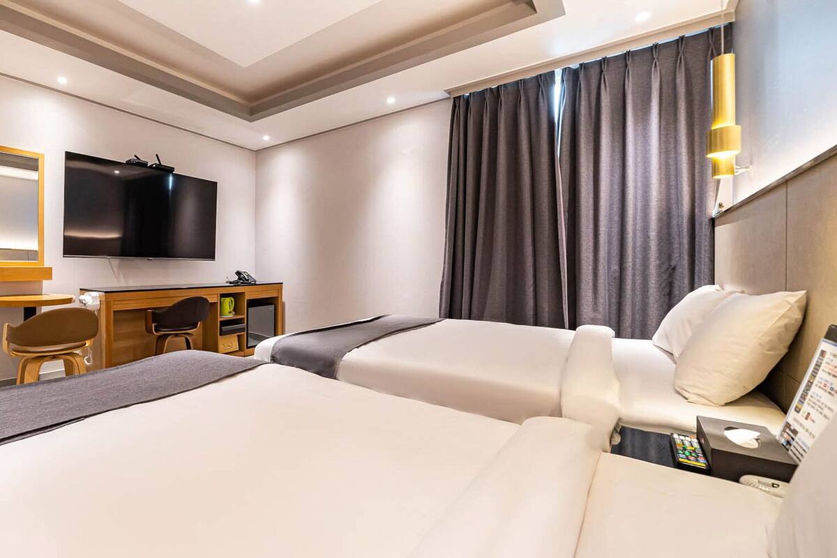 A hotel room with two beds, a desk, a chair, a TV, and a coat rack.