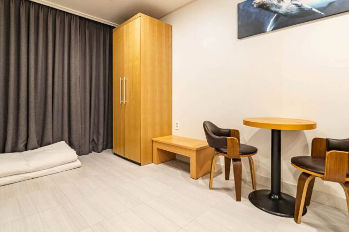 Una habitación con cama, un armario de madera, una mesa redonda con sillas y un banco.