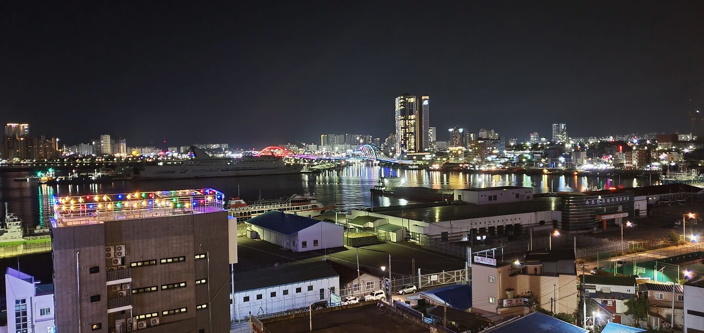 A nighttime cityscape with a prominent bridge, illuminated buildings, and a waterfront area.