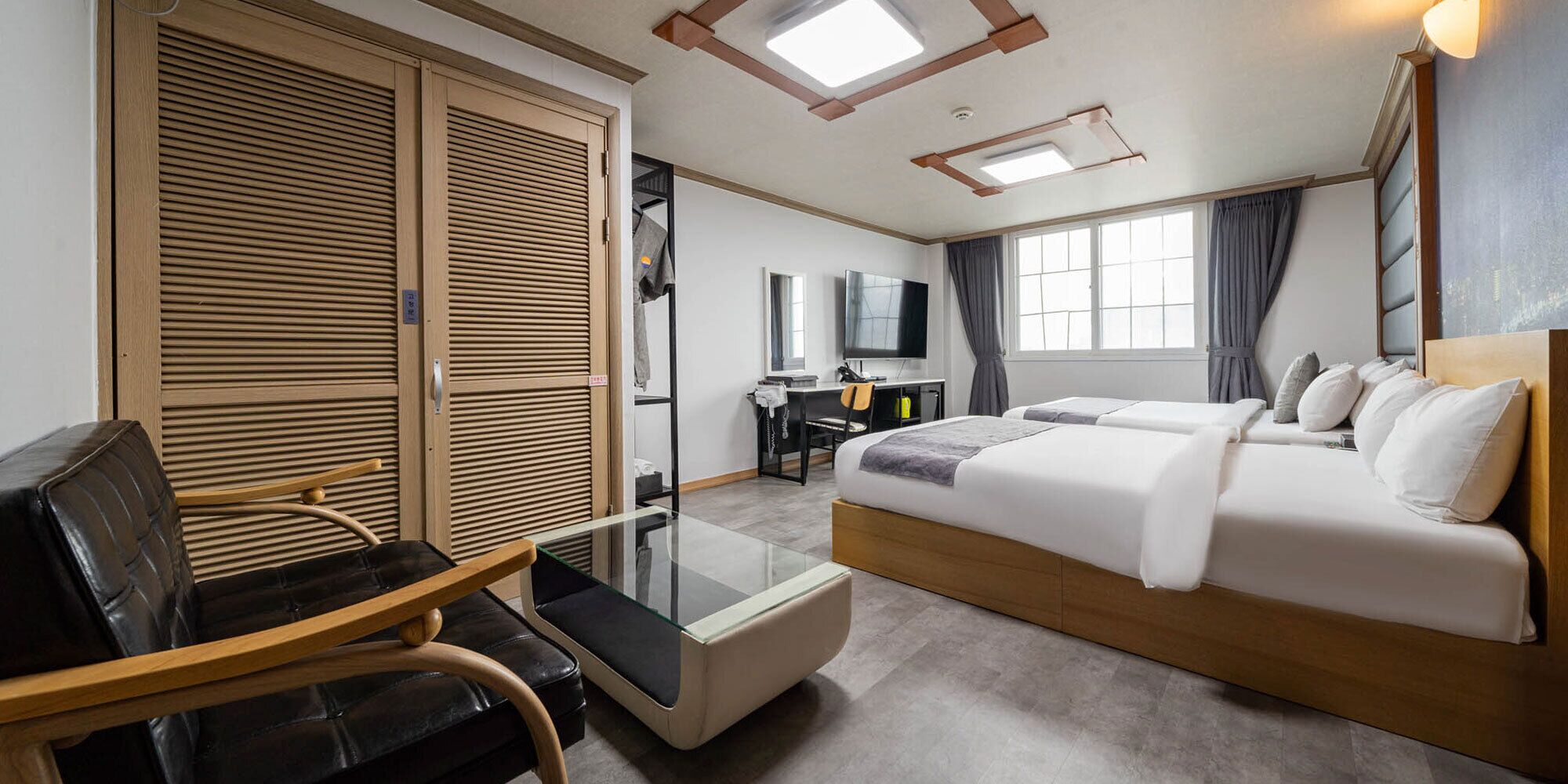 A hotel room with a bed, a desk, a chair, a TV, and a wardrobe.