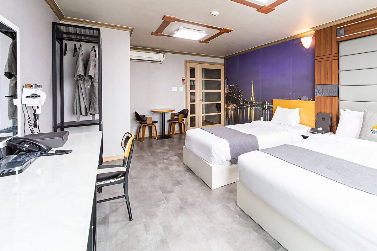 A hotel room with two beds, a desk with a phone, a chair, a small table, and a wardrobe.