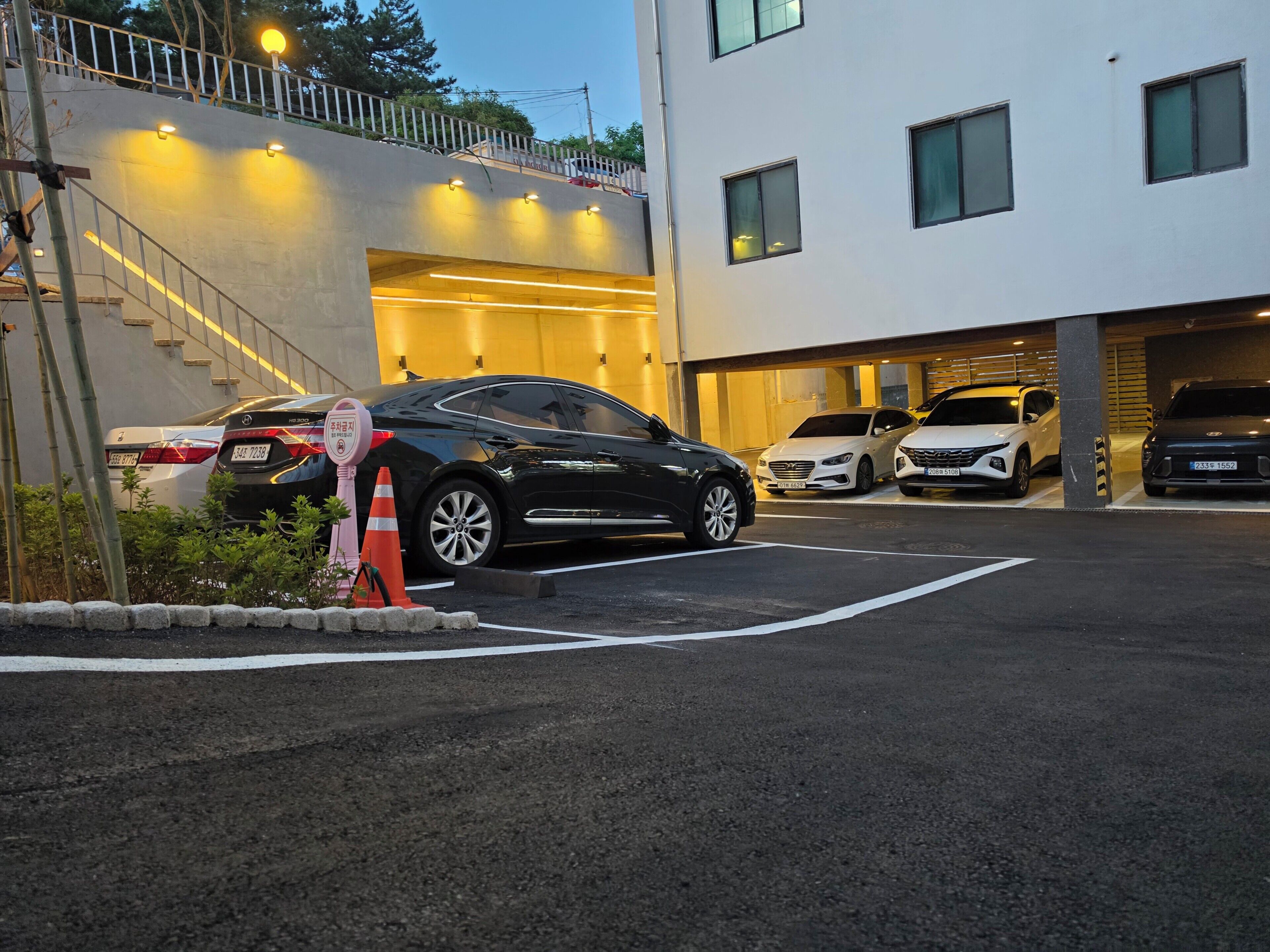 A parking area with cars, a staircase, and a building with multiple windows.