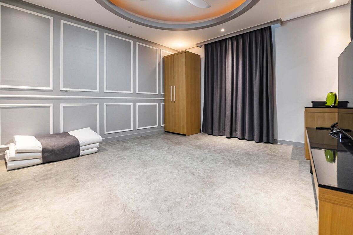 A modern bedroom with a large wardrobe, a bed with white linens, a small table with a lamp, and a large mirror.