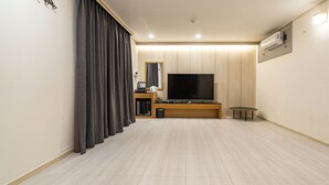 A modern living room with a flat-screen TV, a wooden entertainment unit, a small table, and a large window with curtains. - RITZ HOTEL (Sokcho)