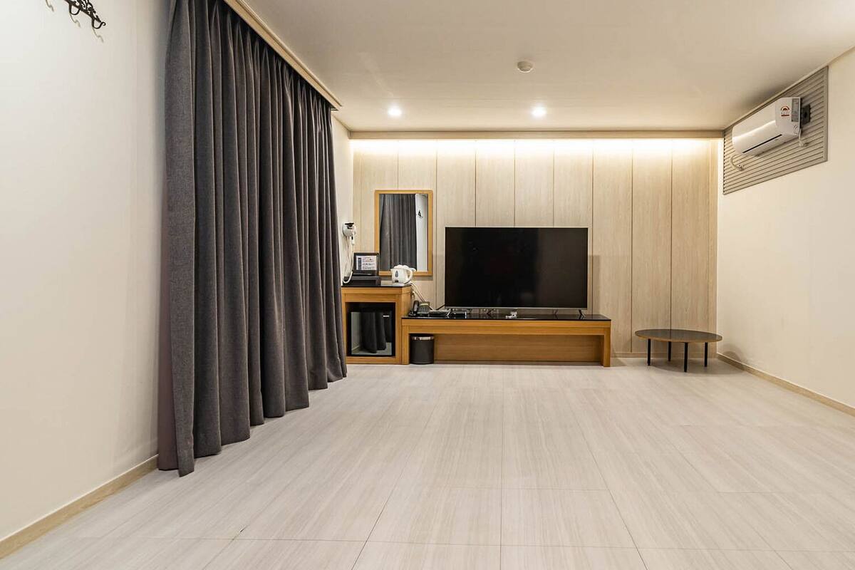 A modern living room with a flat-screen TV, a wooden entertainment unit, a small table, and a large window with curtains.
