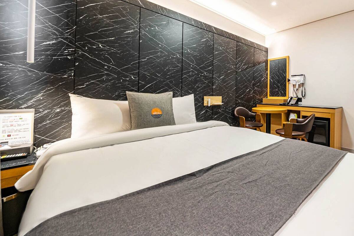 A hotel room with a large bed, a desk, a chair, a robe, and a mirror.