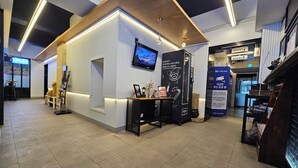 A modern reception area with a white reception desk, a mounted television, and a vending machine. - RITZ HOTEL (Sokcho)