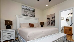 Une chambre à coucher avec un lit blanc, des tables de chevet, une commode, un grand tableau, un miroir et un meuble en bois.